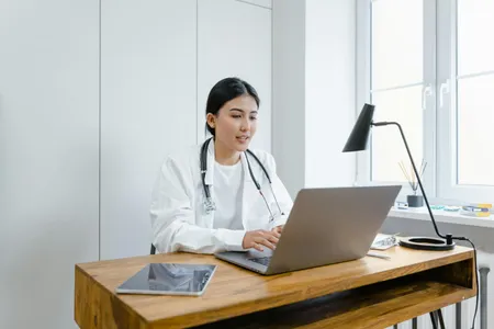 A doctor typing on her laptop with a stethoscope hanging around her neck.