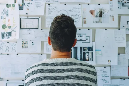 A man looking at a pinboard filled with research papers.